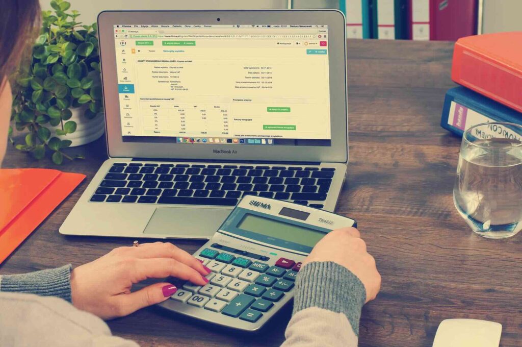 Woman's profile and hands holding large calculator, in front of laptop screen display a spreadsheet - WebGrit