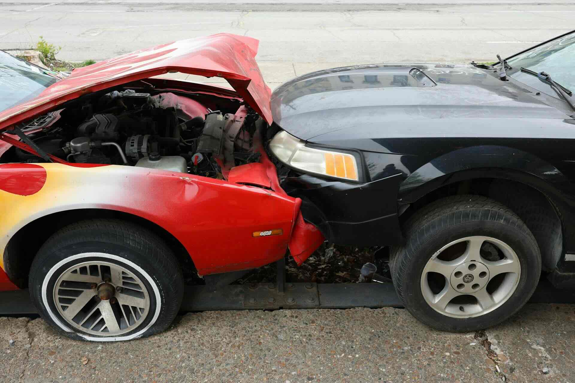 Red car with crumpled hood, rear-ended by black car on street - WebGrit