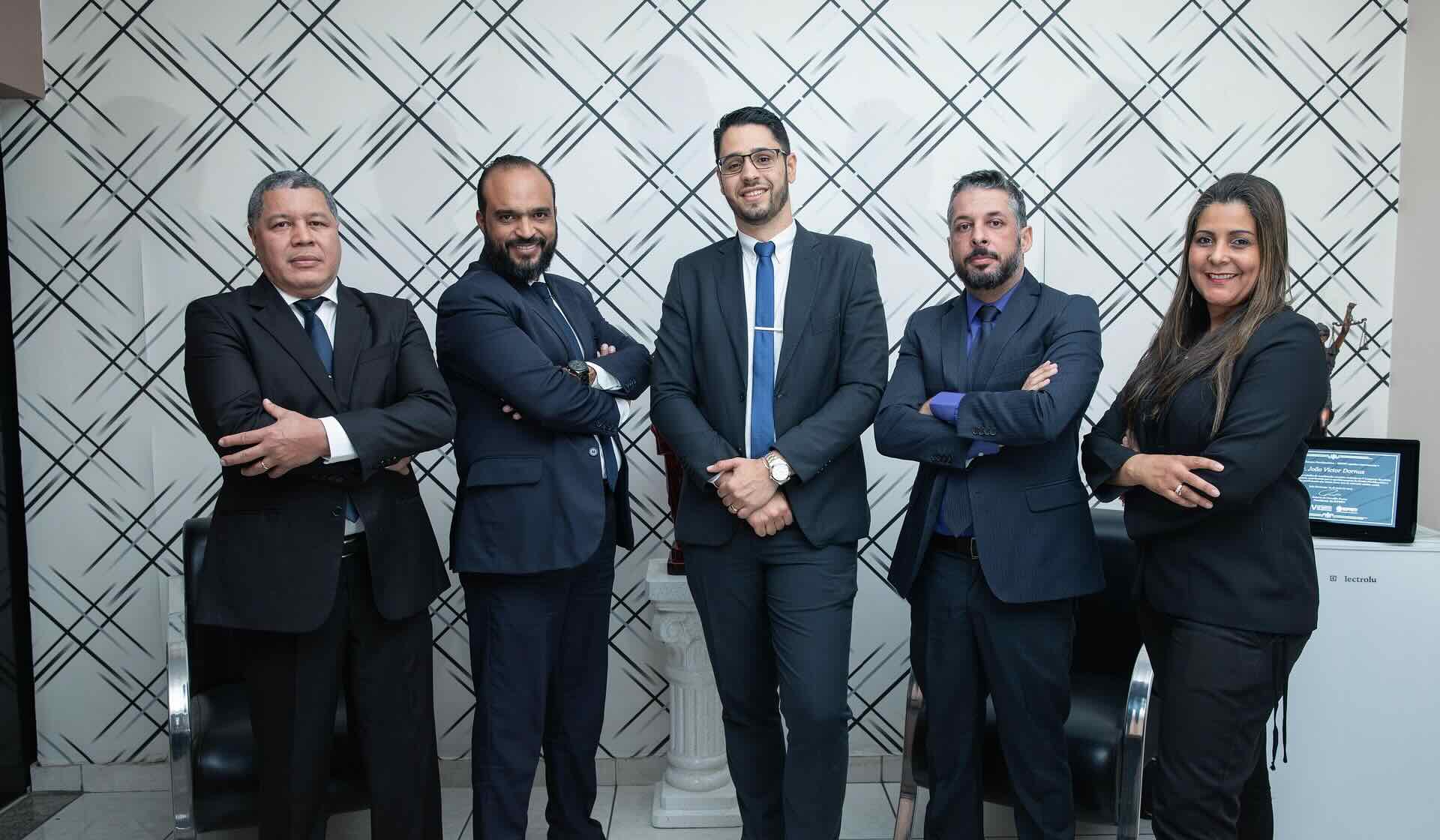 4 smiling men and 1 woman in business attire stand confidently with arms crossed in front of geometric wall pattern - WebGrit
