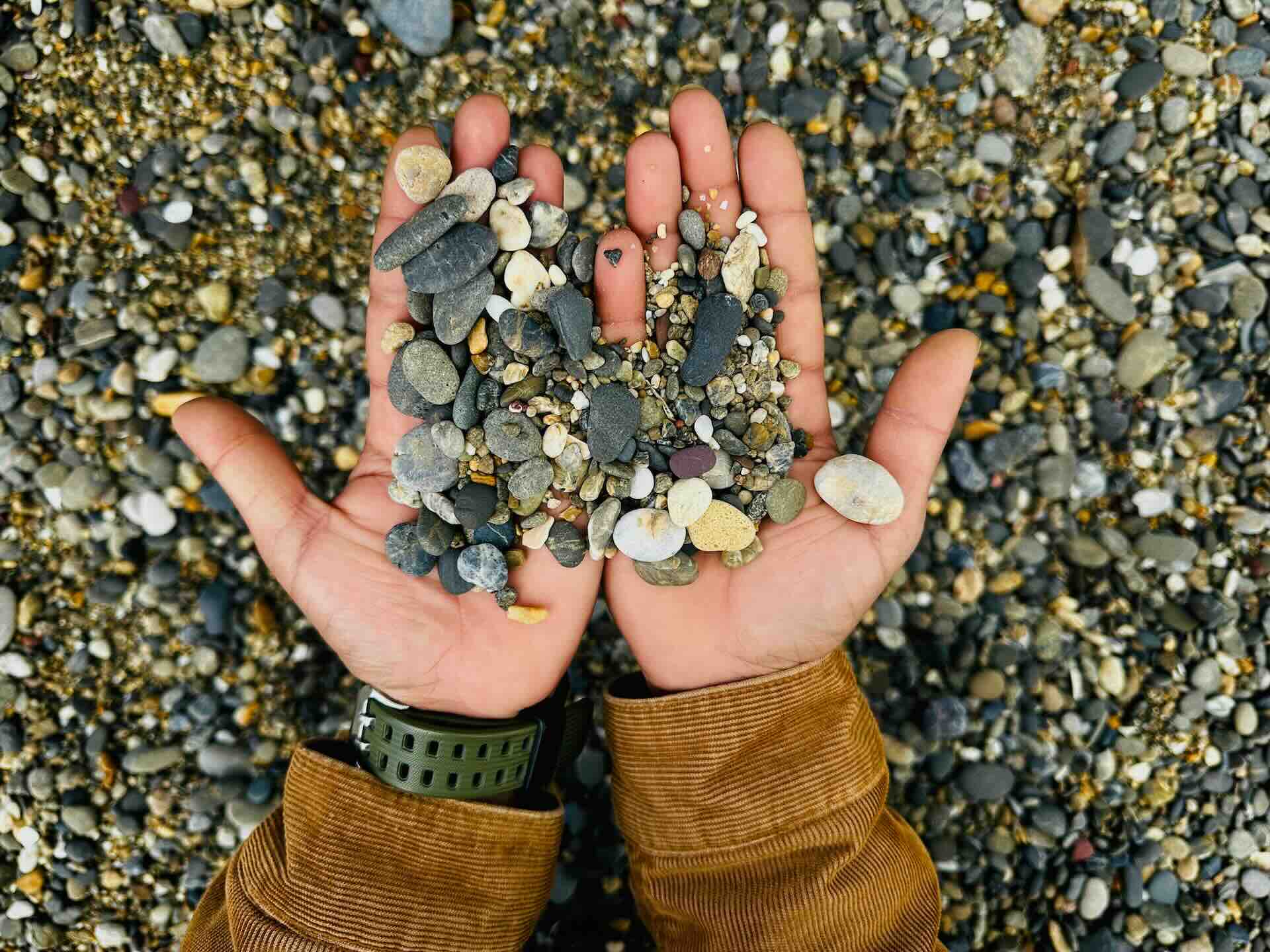 2 hands holding gritty pebbles of varying shapes, sizes, and colors - WebGrit