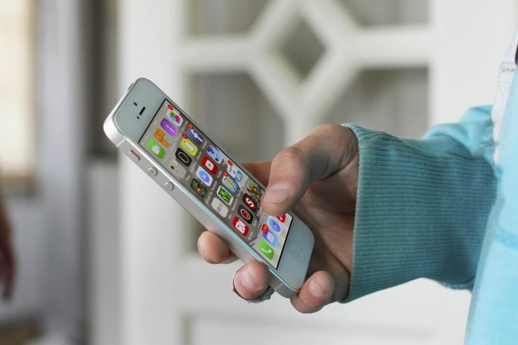 Person's hand holding gray cell phone, screen displaying mobile icons - WebGrit