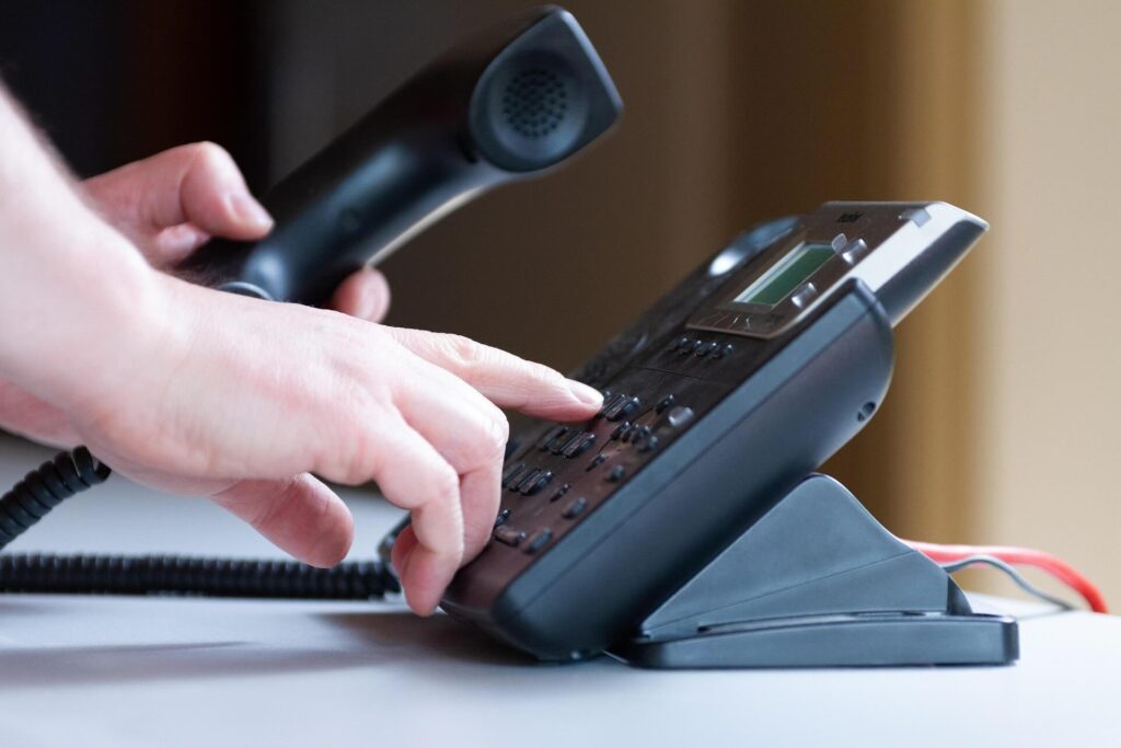 Black telephone, Caucasian person's left hand holding receiver while other hand dials number on telephone - WebGrit